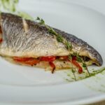Filetto di branzino cucinato, servito su un piatto con contorni freschi e colorati.