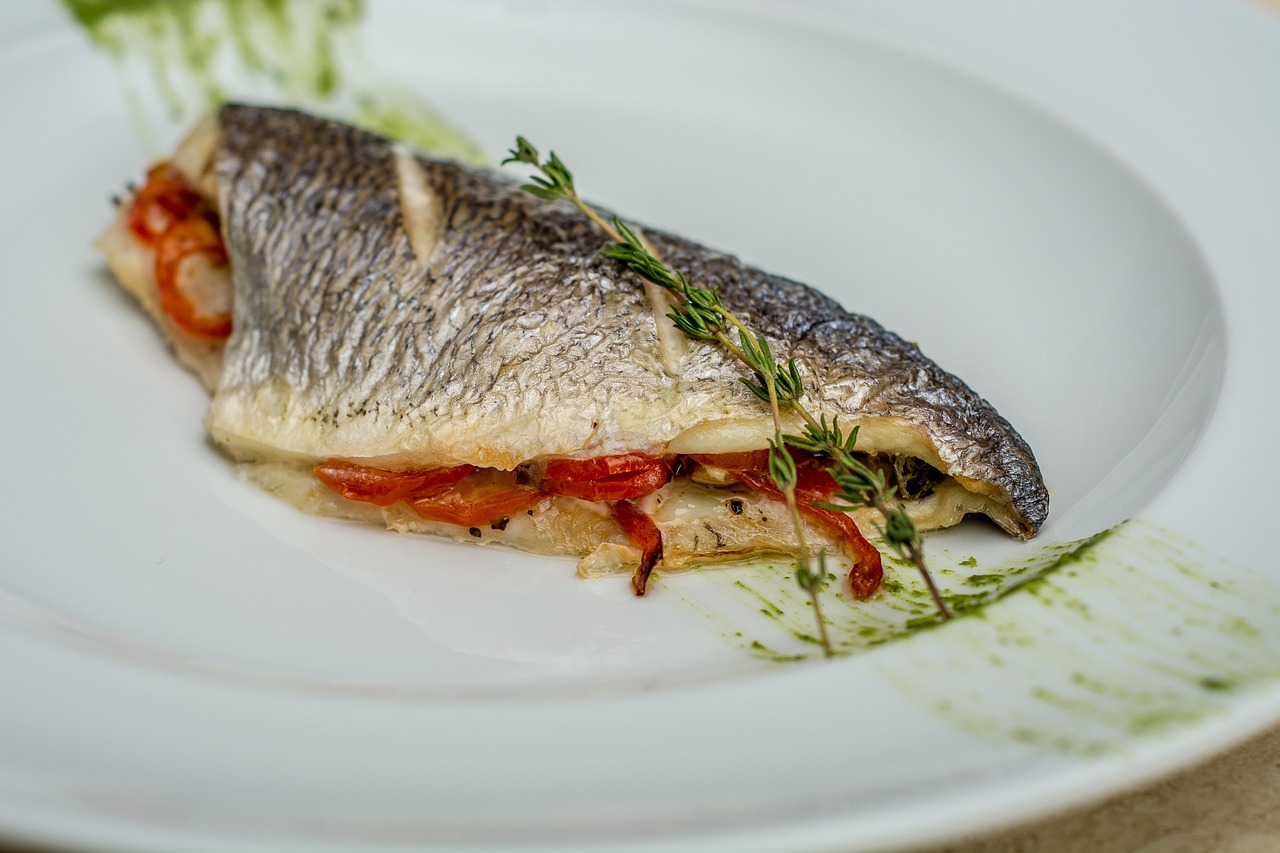 Filetto di branzino cucinato, servito su un piatto con contorni freschi e colorati.