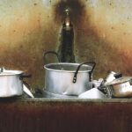 Pentola bruciata con segni di annerimento e utensili per il recupero sul tavolo.